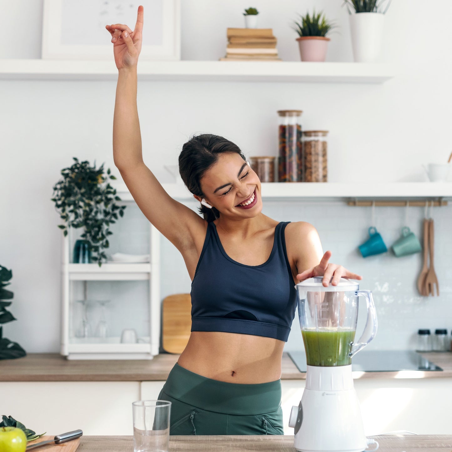 Smiling woman in workout clothes making a smoothie in her kitchen