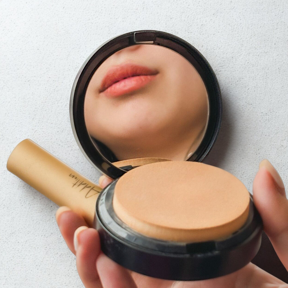 A hand holds the compact makeup powder along with a makeup product beside it