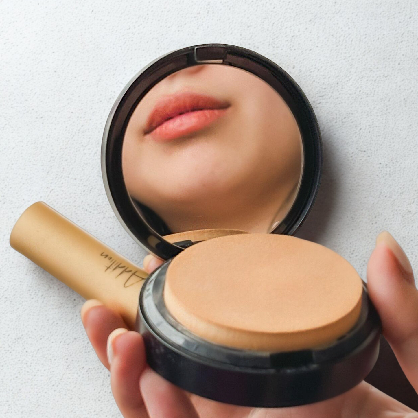 A hand holds the compact makeup powder along with a makeup product beside it