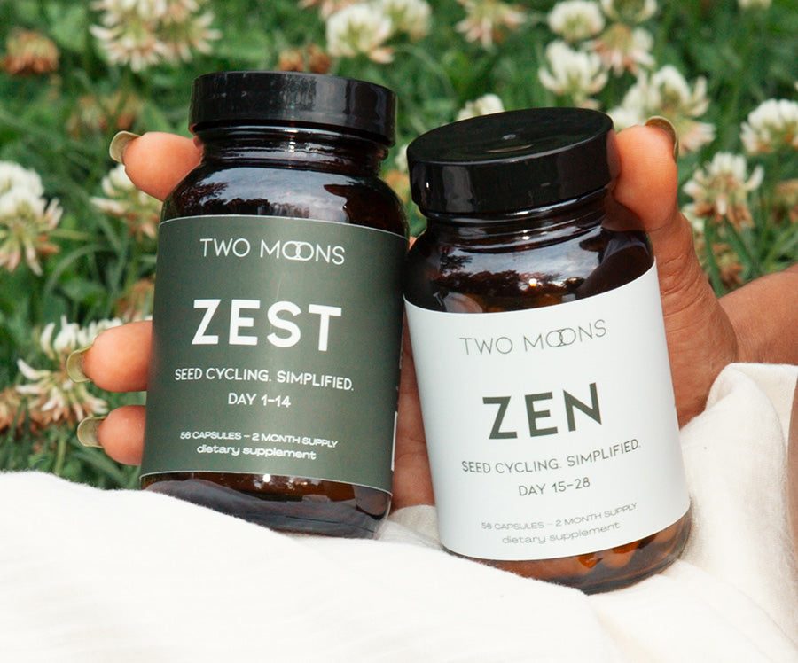 Two bottles labeled 'Zest' and 'Zen' from the brand 'Two Moons' held against a natural background.